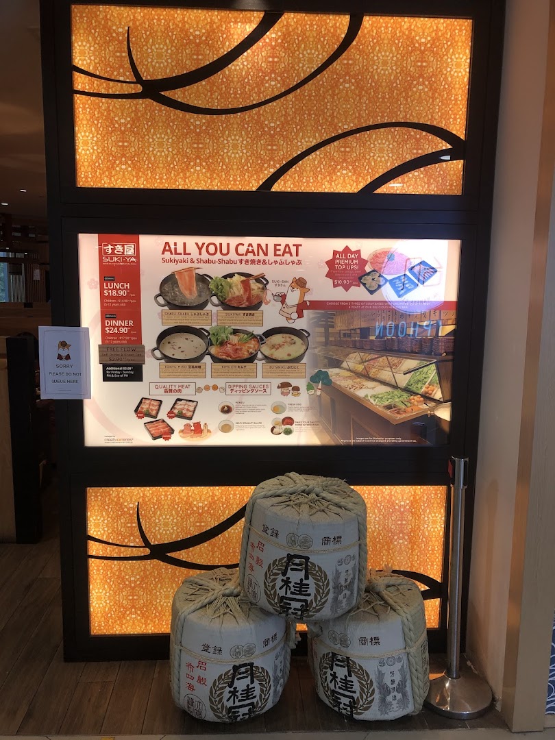 The illuminated shop front of Suki-Ya, an all-you-can-eat shabu-shabu restaurant, featuring menu details and decorative barrels.