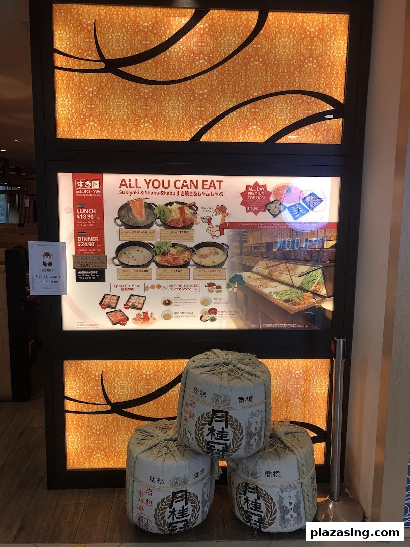 The illuminated shop front of Suki-Ya, an all-you-can-eat shabu-shabu restaurant, featuring menu details and decorative barrels.