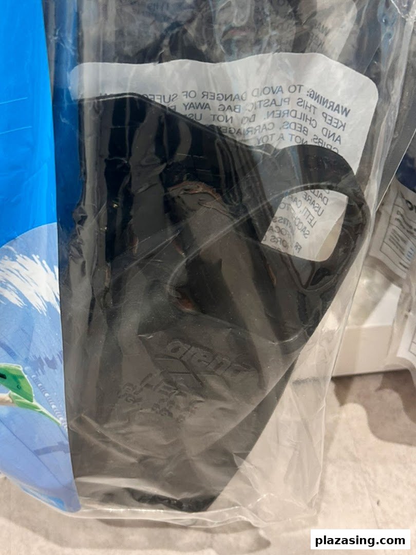 A black swimming fin or flipper is packaged in a clear plastic bag, with a warning label.