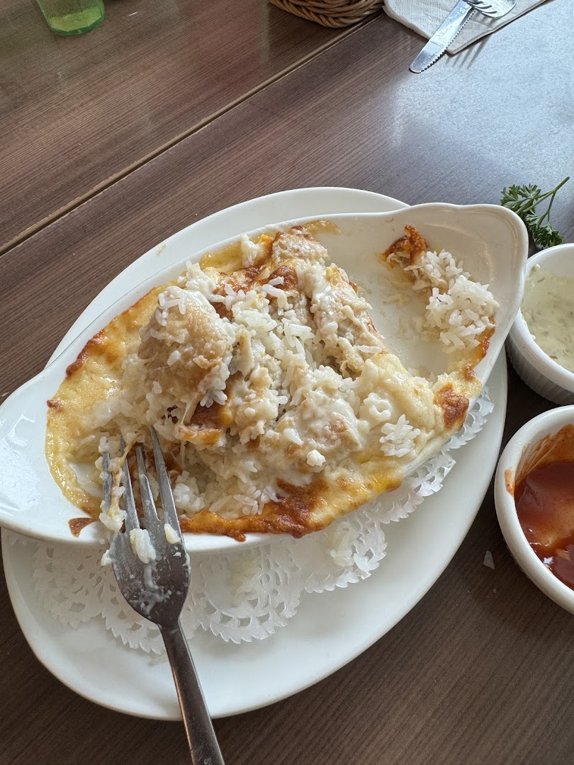 A close-up of a partially eaten baked rice or pasta dish with melted cheese and a fork on a wooden table.