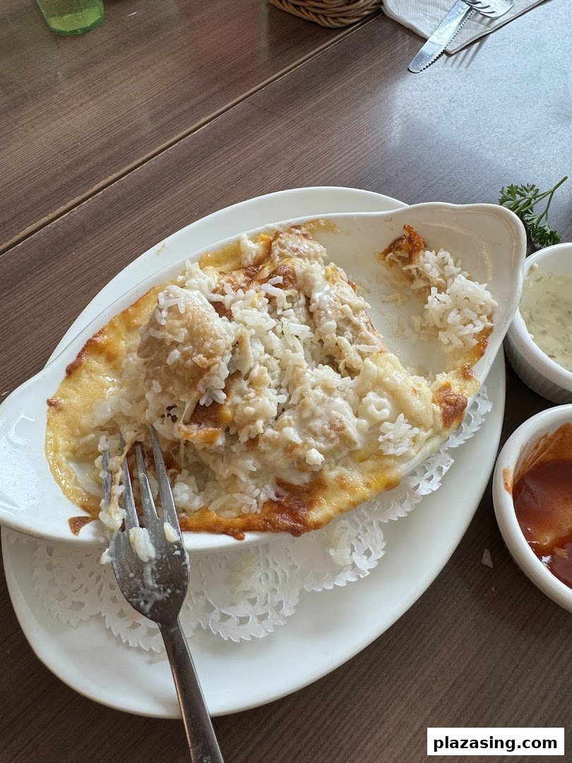 A close-up of a partially eaten baked rice or pasta dish with melted cheese and a fork on a wooden table.