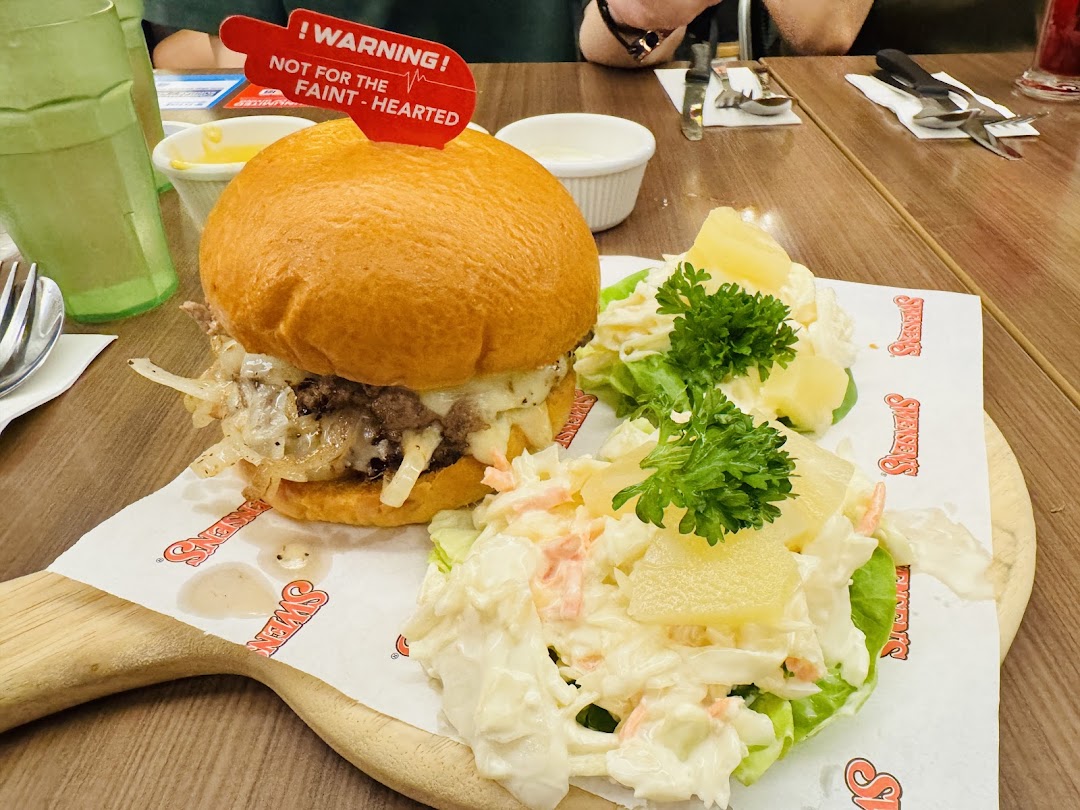 A hearty burger with caramelized onions and cheese, served with coleslaw and pineapple on a wooden board.