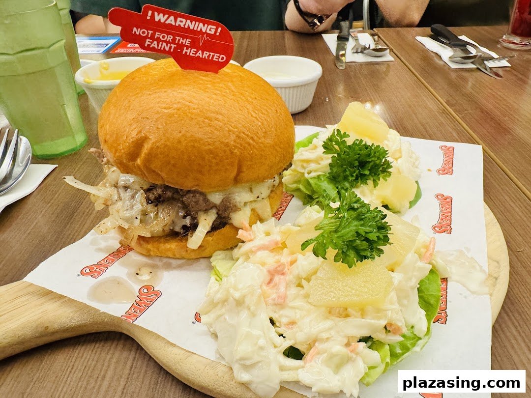 A hearty burger with caramelized onions and cheese, served with coleslaw and pineapple on a wooden board.
