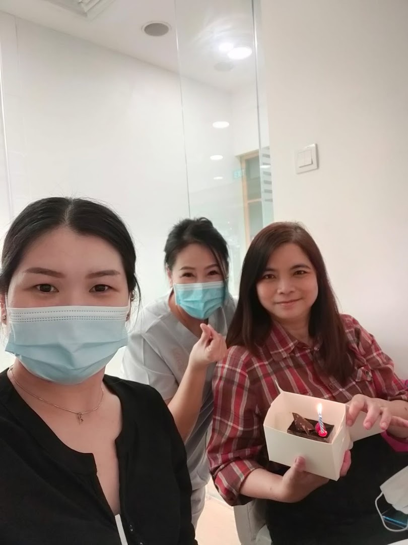 Three women, two masked, celebrate with a small cake and candle in a bright indoor setting.