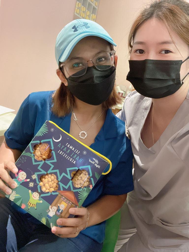 Two women pose with a festive Hari Raya gift box filled with delicious snacks.