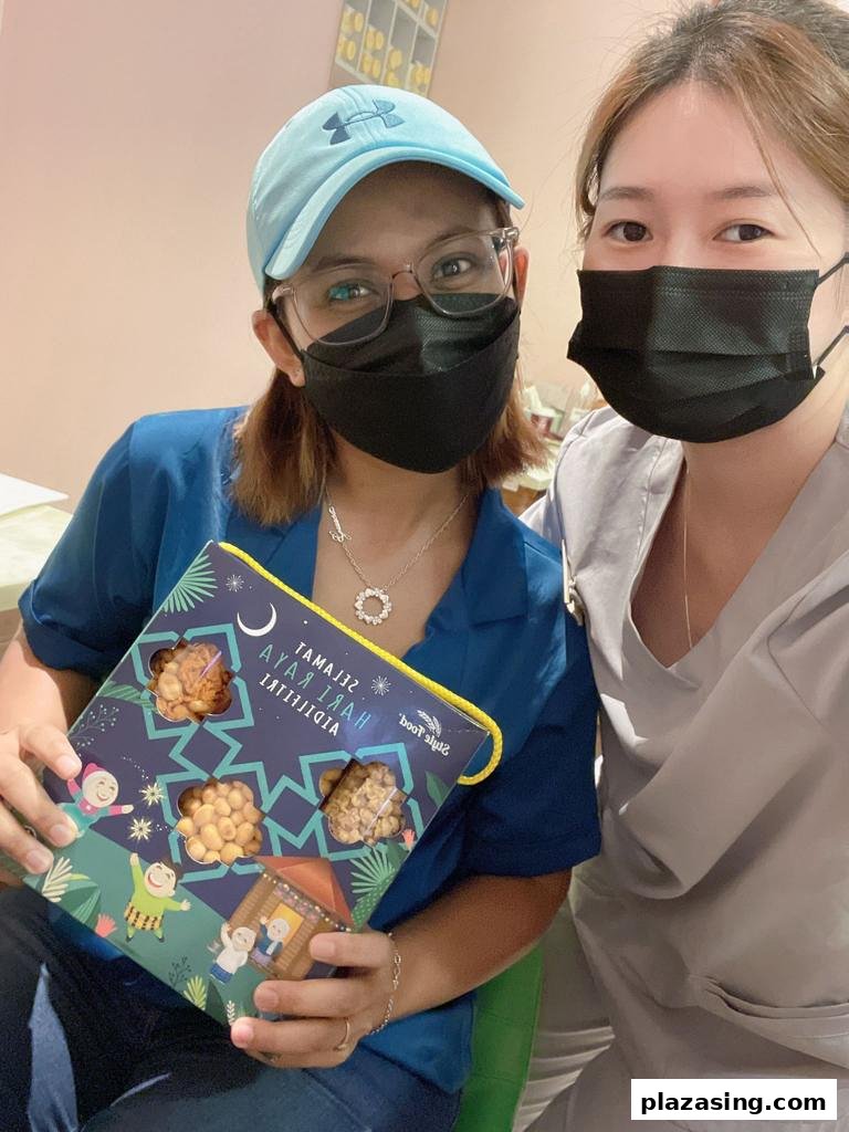 Two women pose with a festive Hari Raya gift box filled with delicious snacks.
