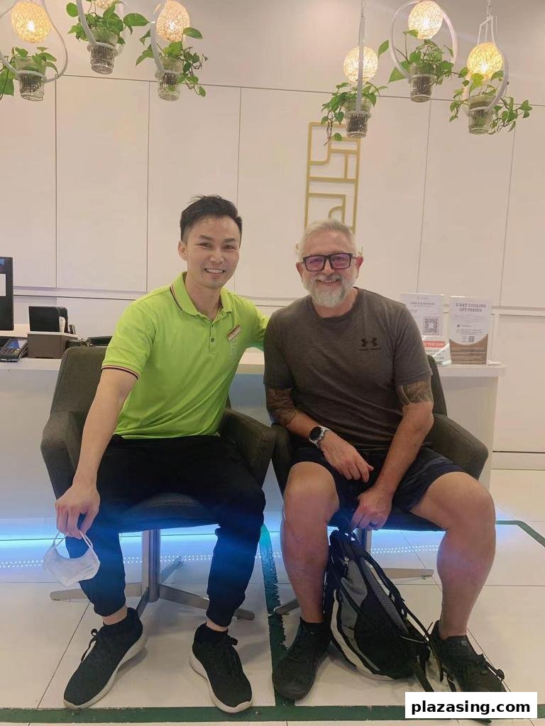 Two men smiling, seated in a bright, modern reception area with hanging plants.
