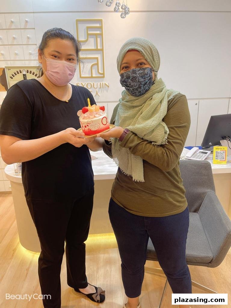 Two masked women, one staff and one customer, holding a small birthday cake inside Syoujin shop.
