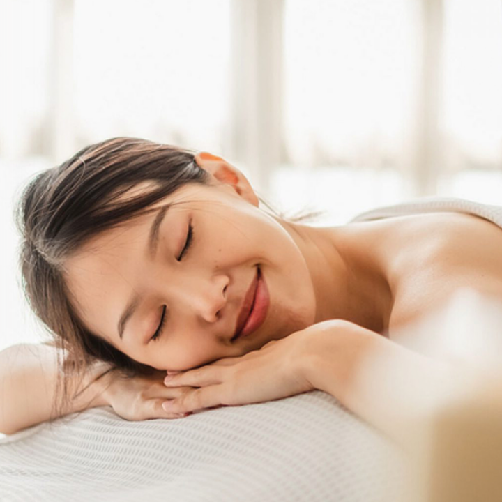 A woman with eyes closed, smiling serenely, enjoying a relaxing spa or beauty treatment.