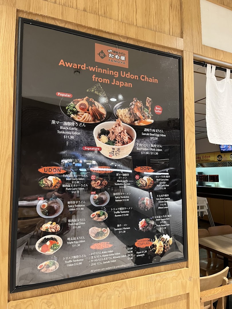 A large, illuminated menu board showcasing various udon, ramen, donburi, and tempura dishes with prices and photos.