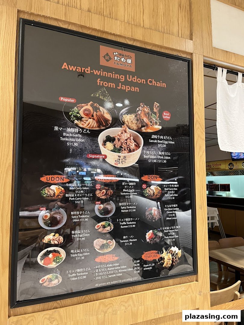 A large, illuminated menu board showcasing various udon, ramen, donburi, and tempura dishes with prices and photos.