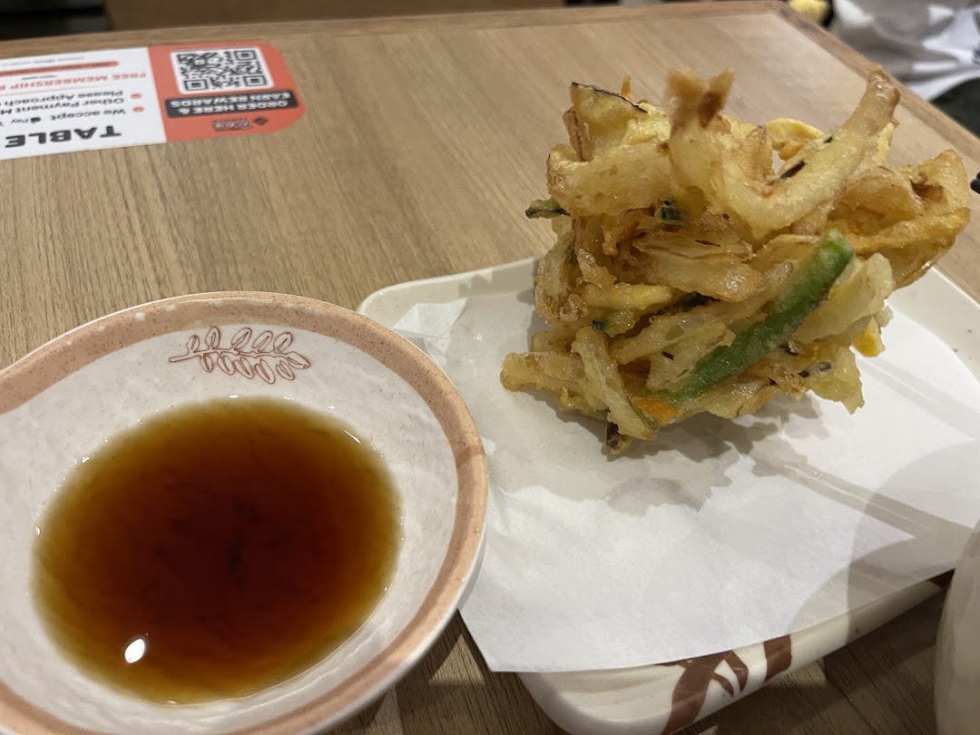 Crispy vegetable tempura with dipping sauce served on a wooden table at Tamoya Udon.