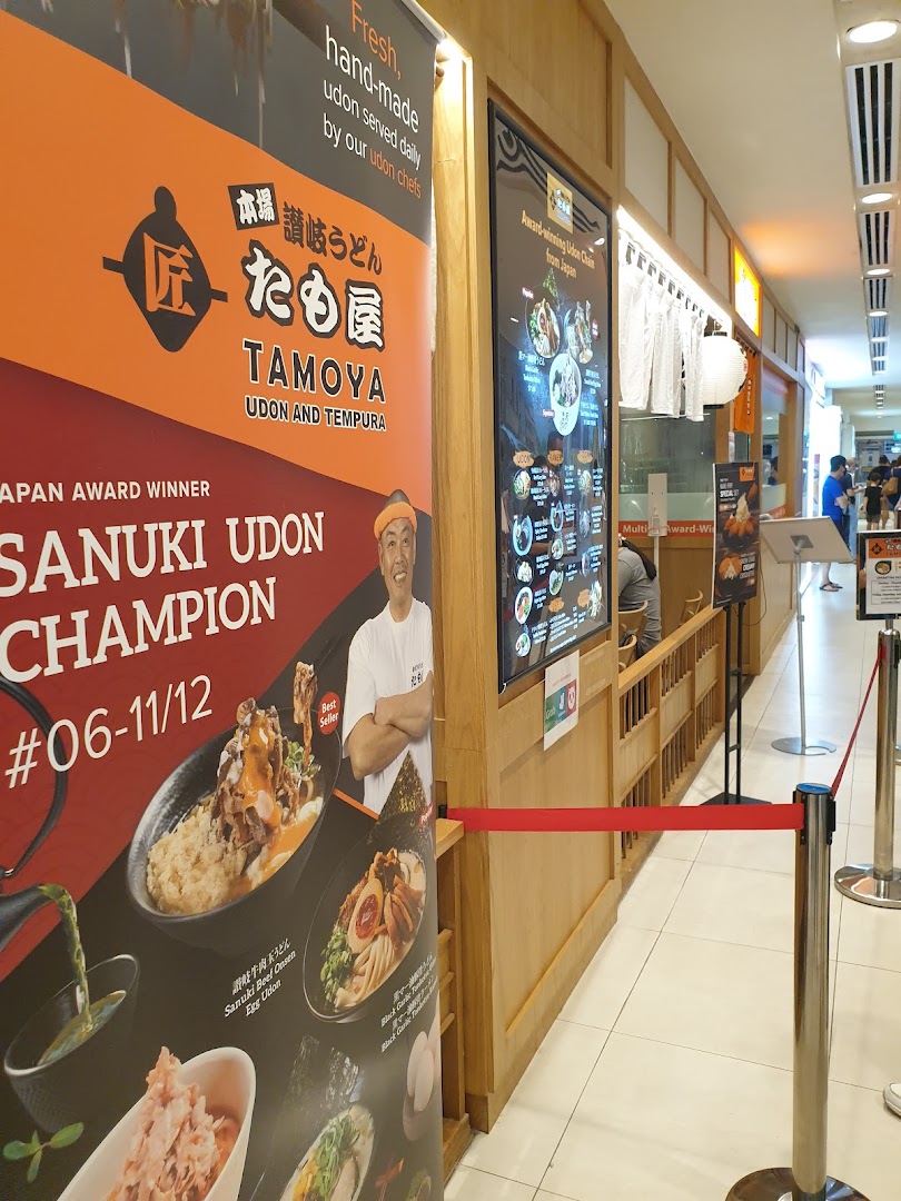 The entrance of Tamoya Udon & Tempura, featuring a large promotional banner and digital menu board.