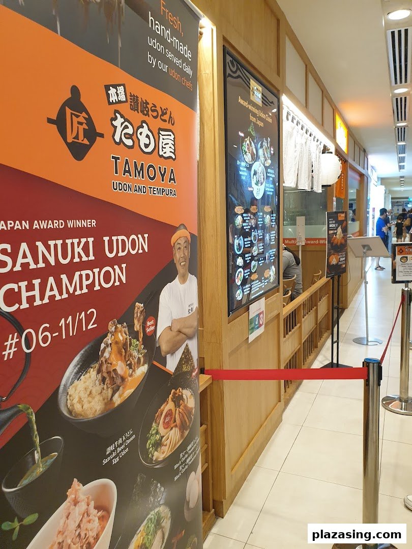 The entrance of Tamoya Udon & Tempura, featuring a large promotional banner and digital menu board.