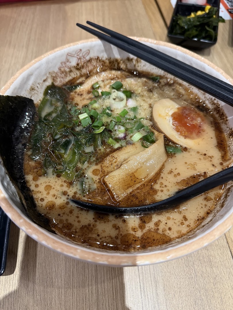 A close-up of a rich, flavorful bowl of ramen or udon with egg, seaweed, and scallions.