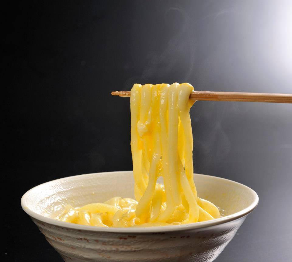 Chopsticks lifting steaming, thick udon noodles from a bowl, coated in a rich, yellow sauce.