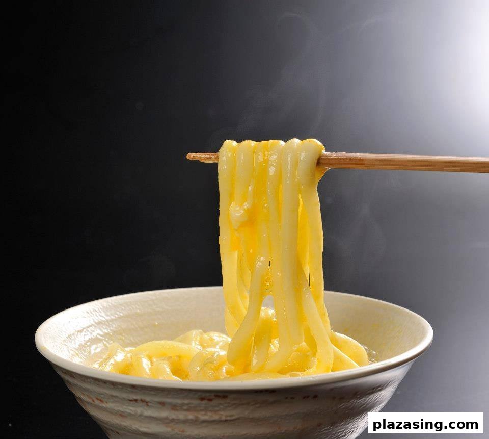 Chopsticks lifting steaming, thick udon noodles from a bowl, coated in a rich, yellow sauce.