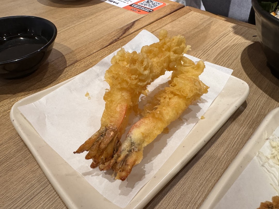 Two golden-fried shrimp tempura pieces served on a white paper-lined plate.