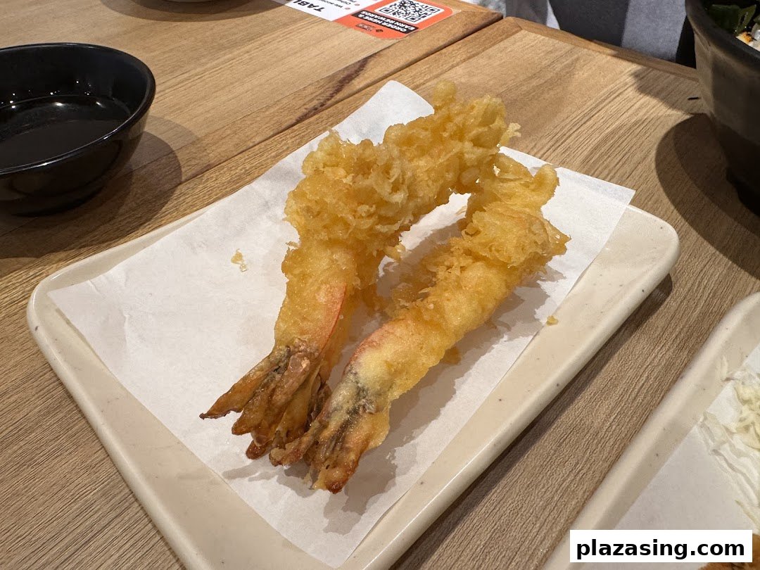 Two golden-fried shrimp tempura pieces served on a white paper-lined plate.