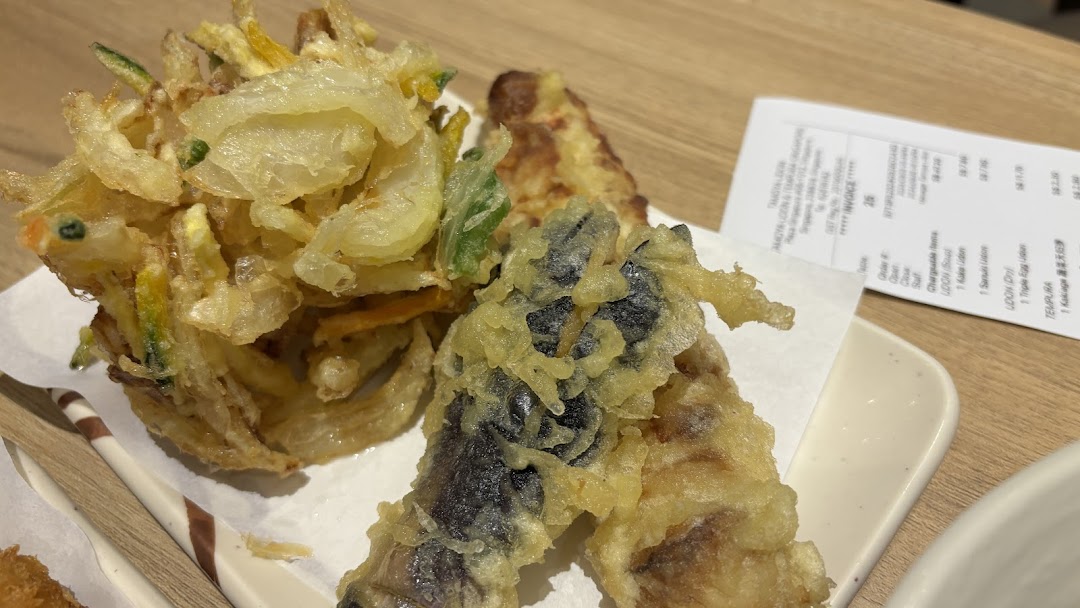 A close-up of freshly fried tempura dishes, including kakiage and other vegetables, served on a white plate.