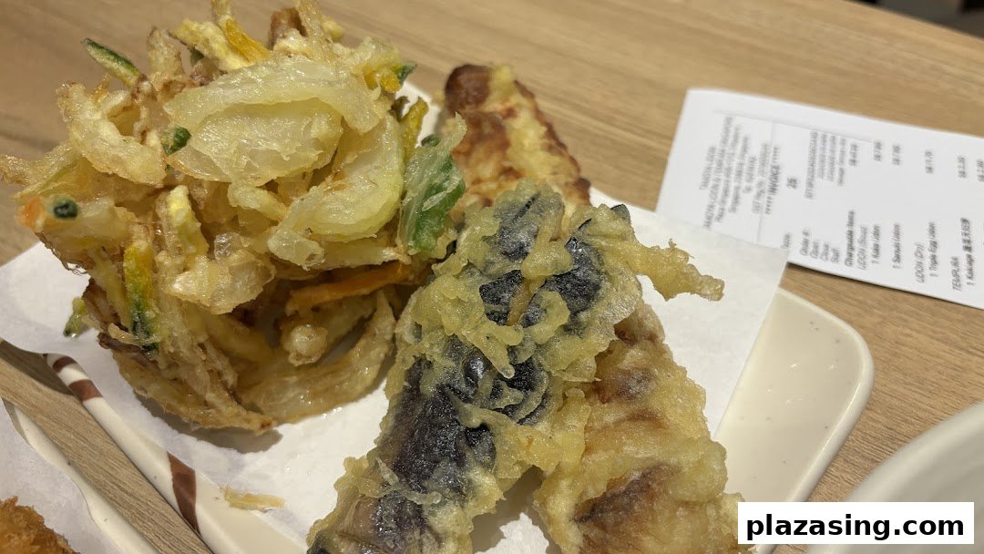 A close-up of freshly fried tempura dishes, including kakiage and other vegetables, served on a white plate.