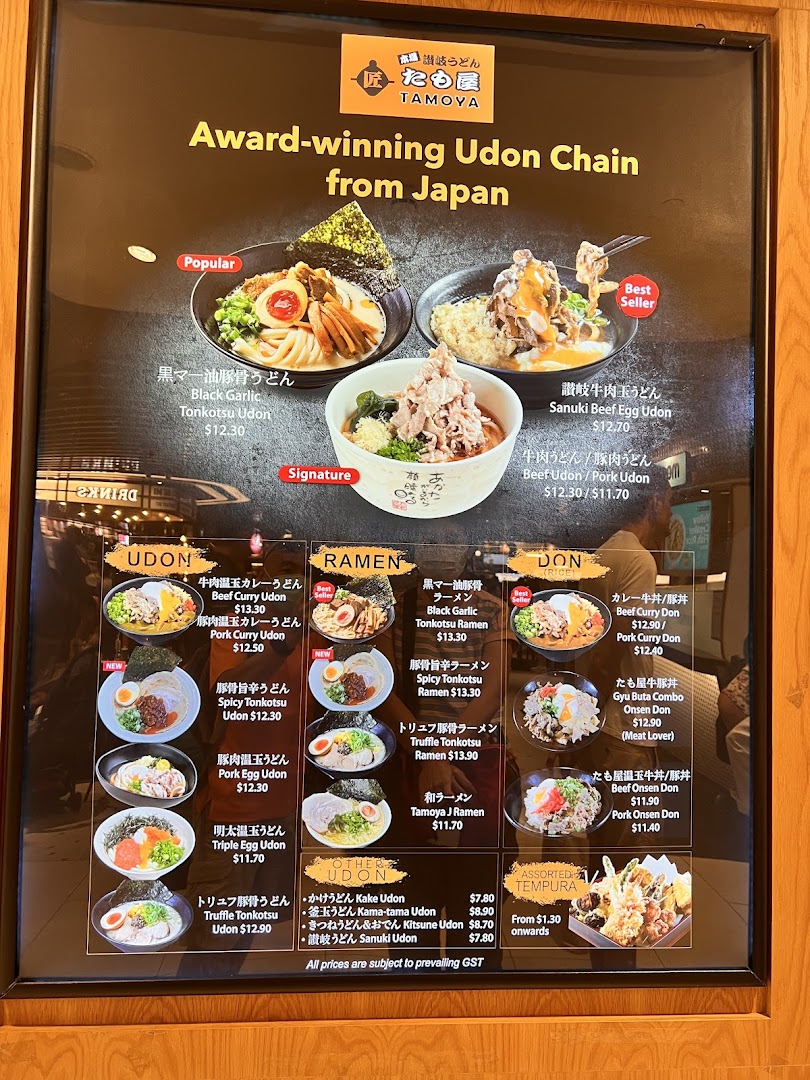A large menu board for Tamoya Udon, showcasing various Japanese udon, ramen, donburi, and tempura dishes with prices.