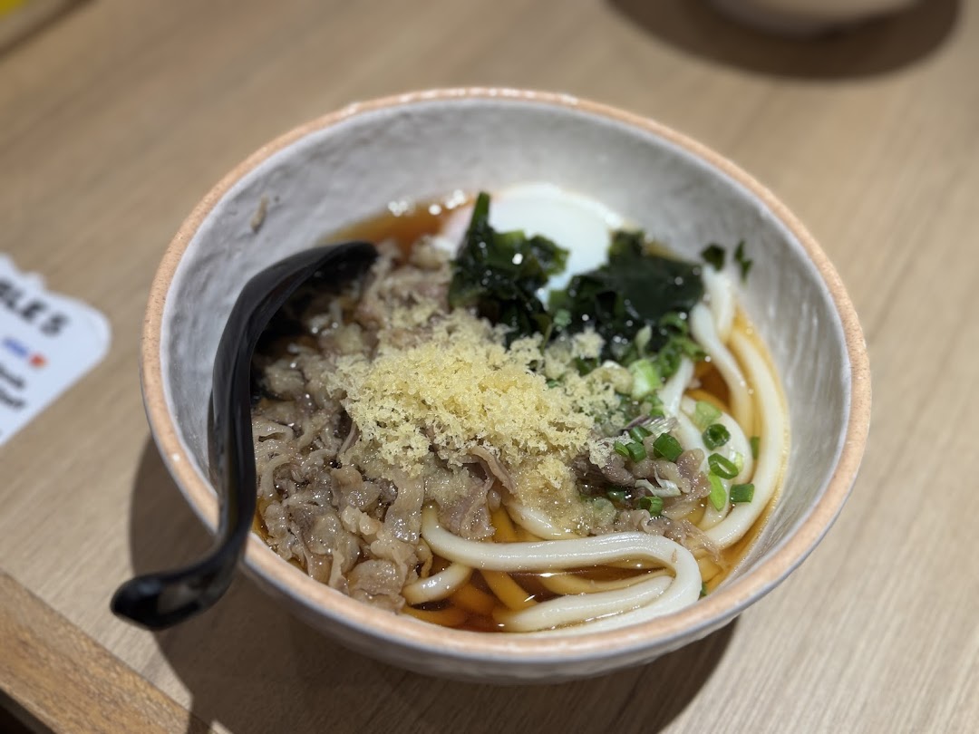 A close-up of a delicious bowl of udon noodles with beef, egg, and seaweed.