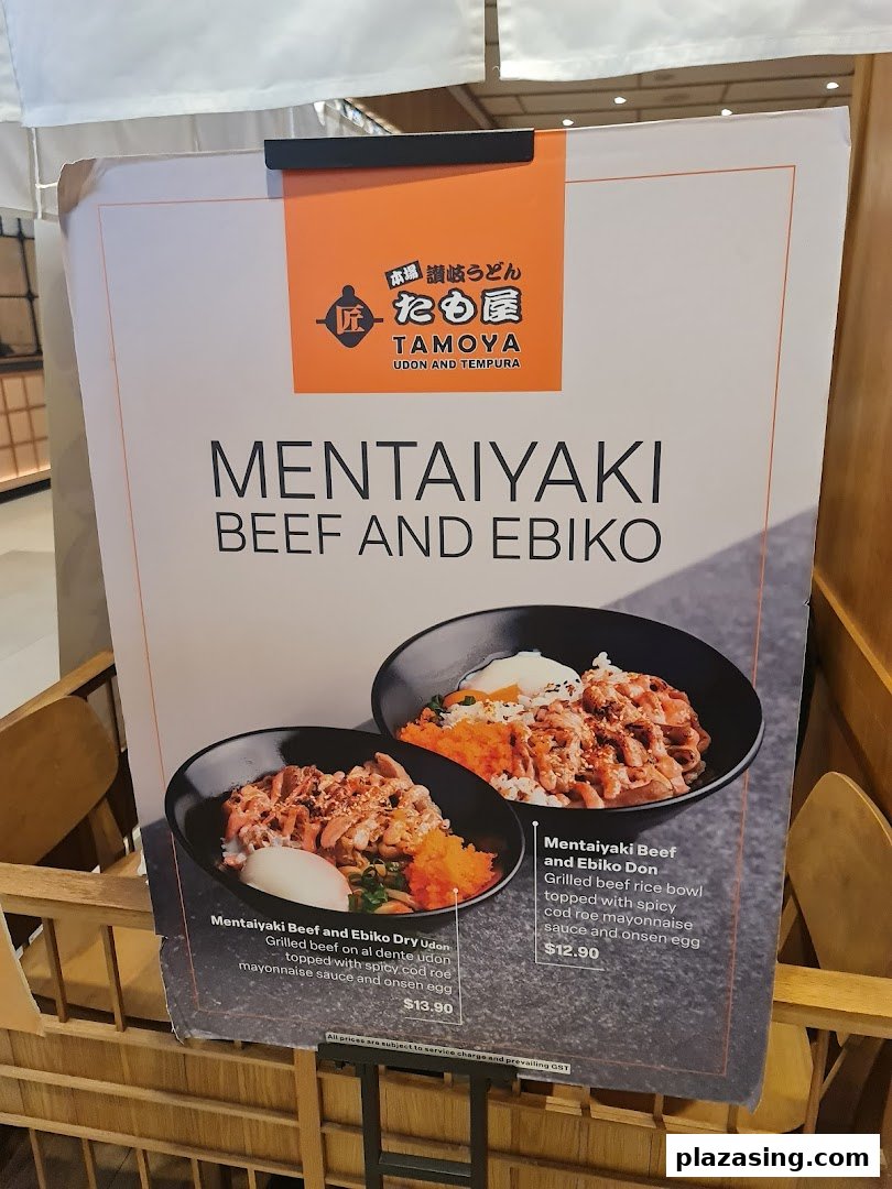 A promotional stand for Tamoya Udon featuring Mentaikyaki Beef and Ebiko dishes with prices.