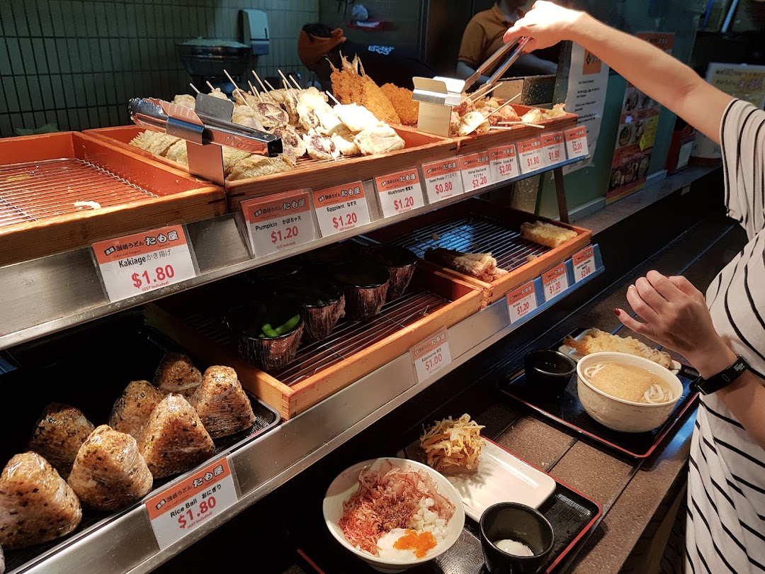 A customer selects freshly prepared tempura and udon at a Japanese food counter.
