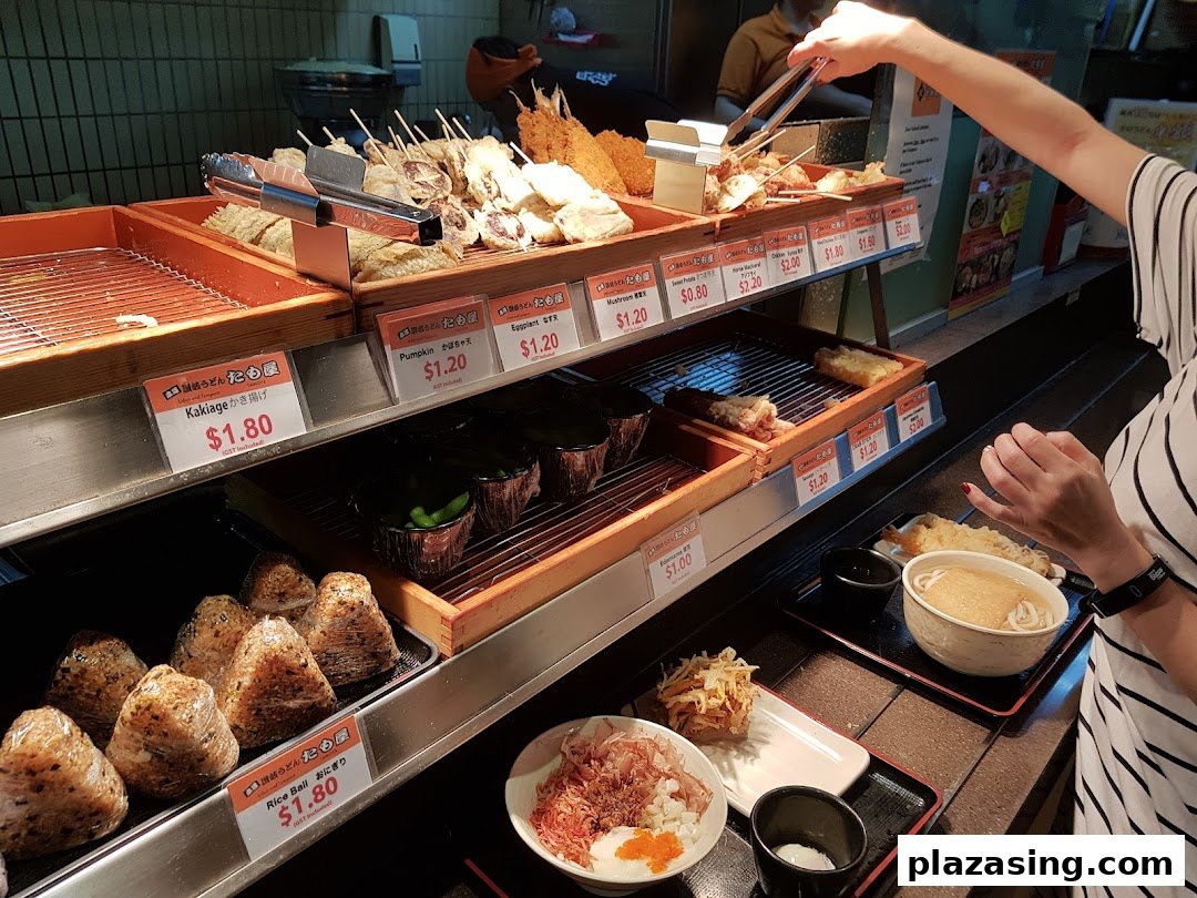 A customer selects freshly prepared tempura and udon at a Japanese food counter.