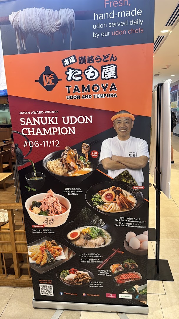 A promotional standee for Tamoya Udon & Tempura, featuring award-winning udon dishes and a smiling chef.