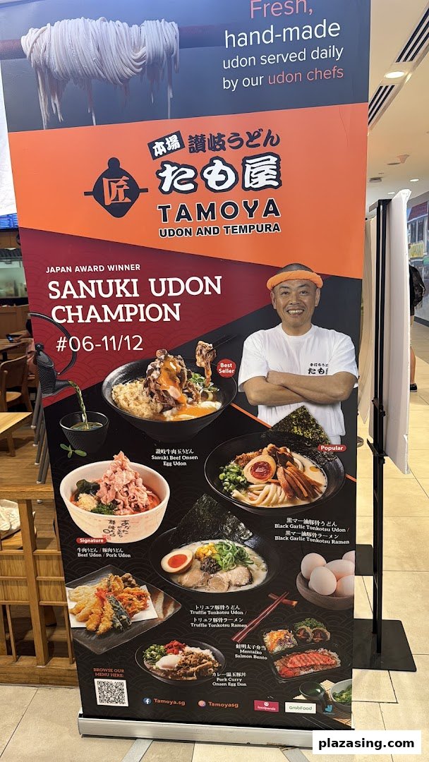 A promotional standee for Tamoya Udon & Tempura, featuring award-winning udon dishes and a smiling chef.