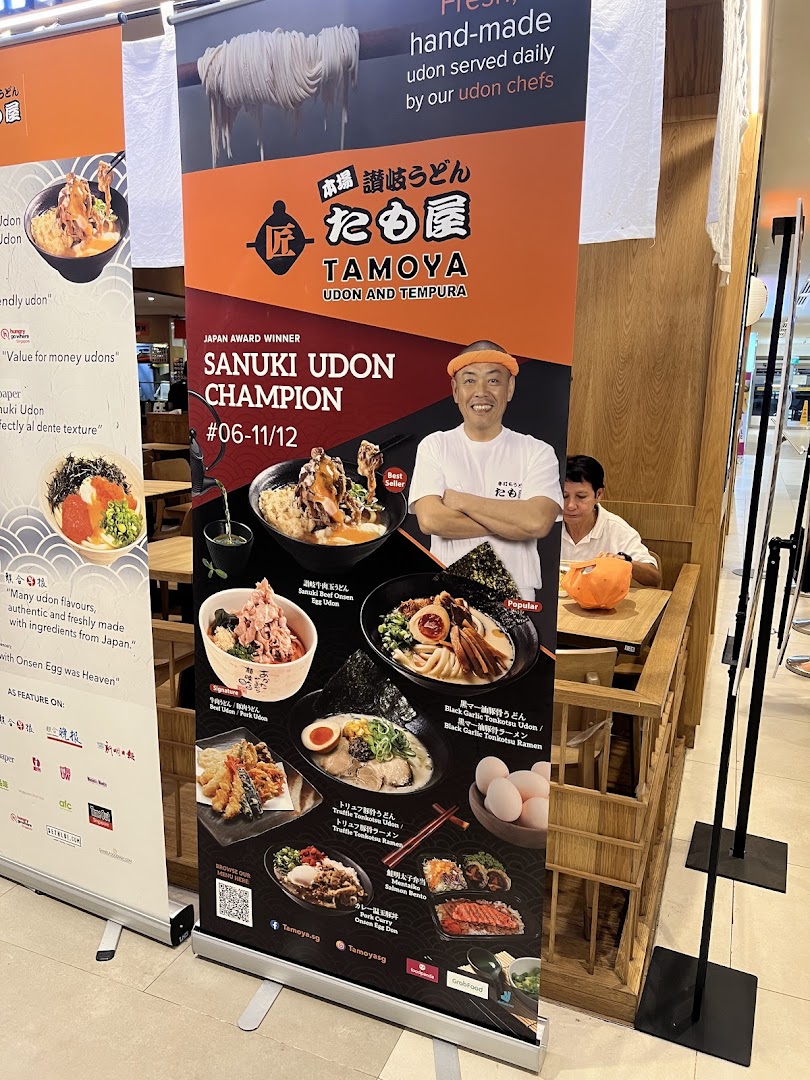 A large promotional standee for Tamoya Udon & Tempura, showcasing various dishes and a smiling chef.