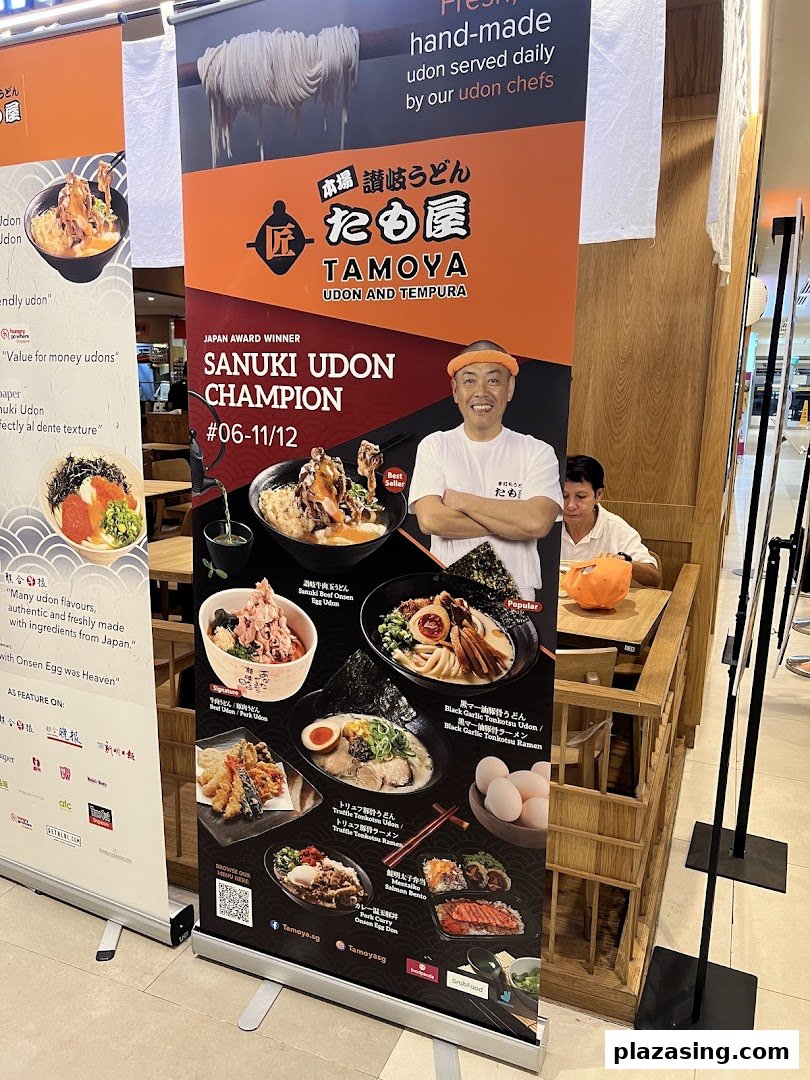 A large promotional standee for Tamoya Udon & Tempura, showcasing various dishes and a smiling chef.