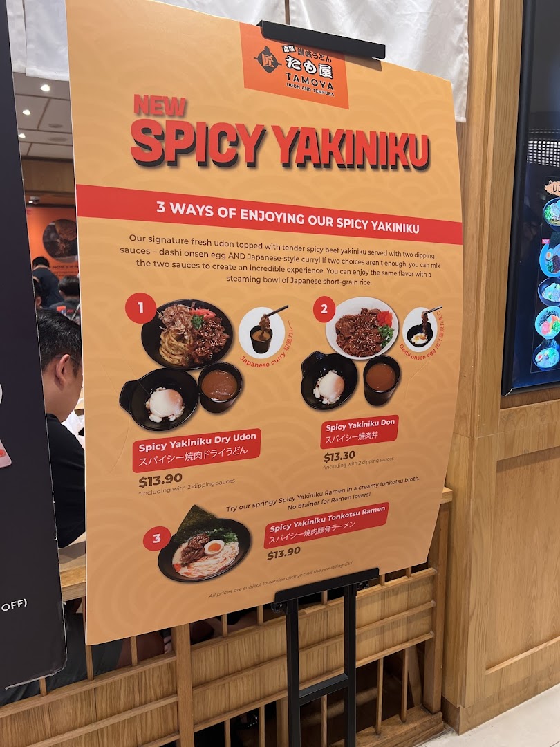 A promotional standee showcasing Tamoya Udon's new 'Spicy Yakiniku' dishes with prices and descriptions.