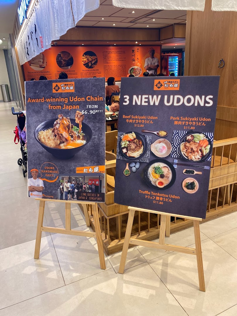 Two promotional standees outside Tamoya Udon Tempura, showcasing award-winning udon and new menu items.