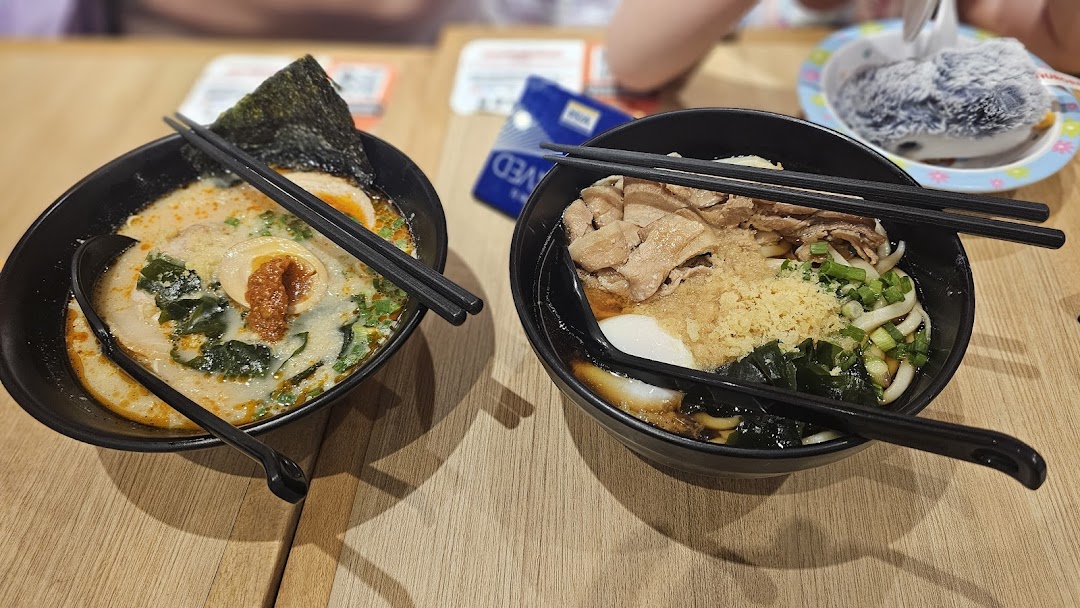 Two bowls of delicious Japanese noodles, one ramen and one udon, served on a wooden table.