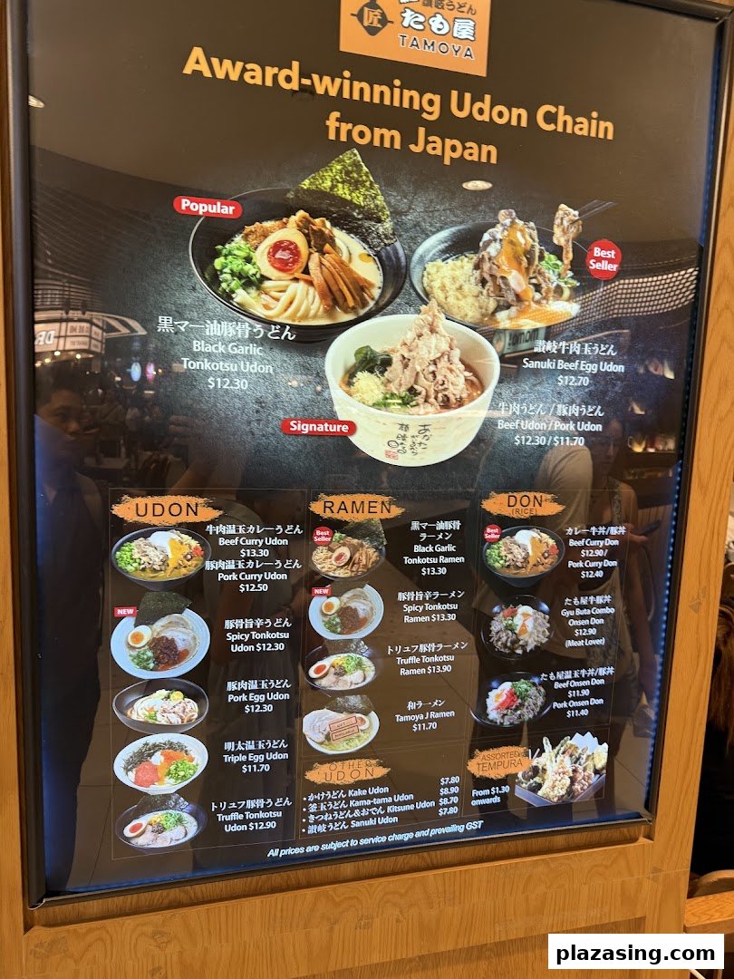 A brightly lit menu board showcasing a variety of udon, ramen, donburi, and tempura dishes with prices.