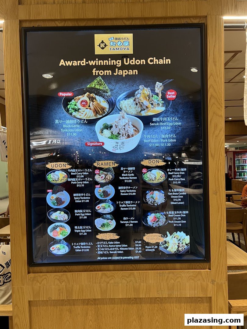 A digital menu board displaying various udon, ramen, donburi, and tempura dishes with prices and images.