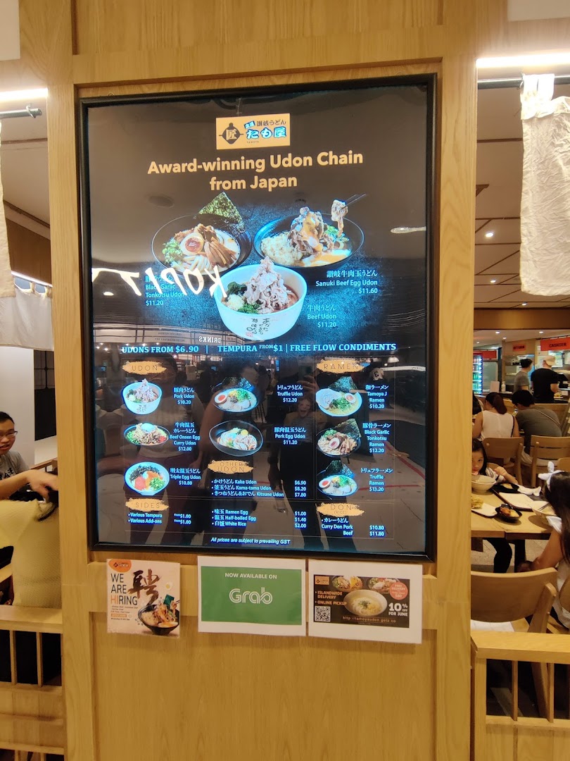 A digital menu board displaying various Japanese udon, ramen, and rice bowl dishes with prices and promotions.