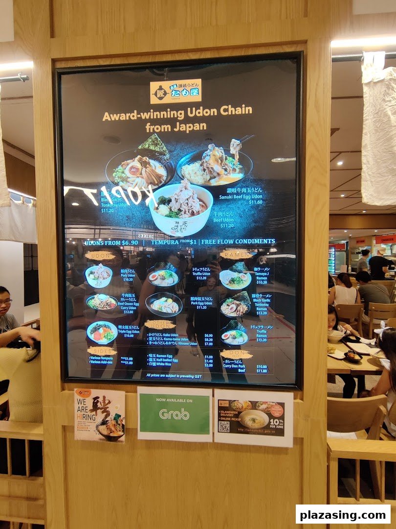 A digital menu board displaying various Japanese udon, ramen, and rice bowl dishes with prices and promotions.