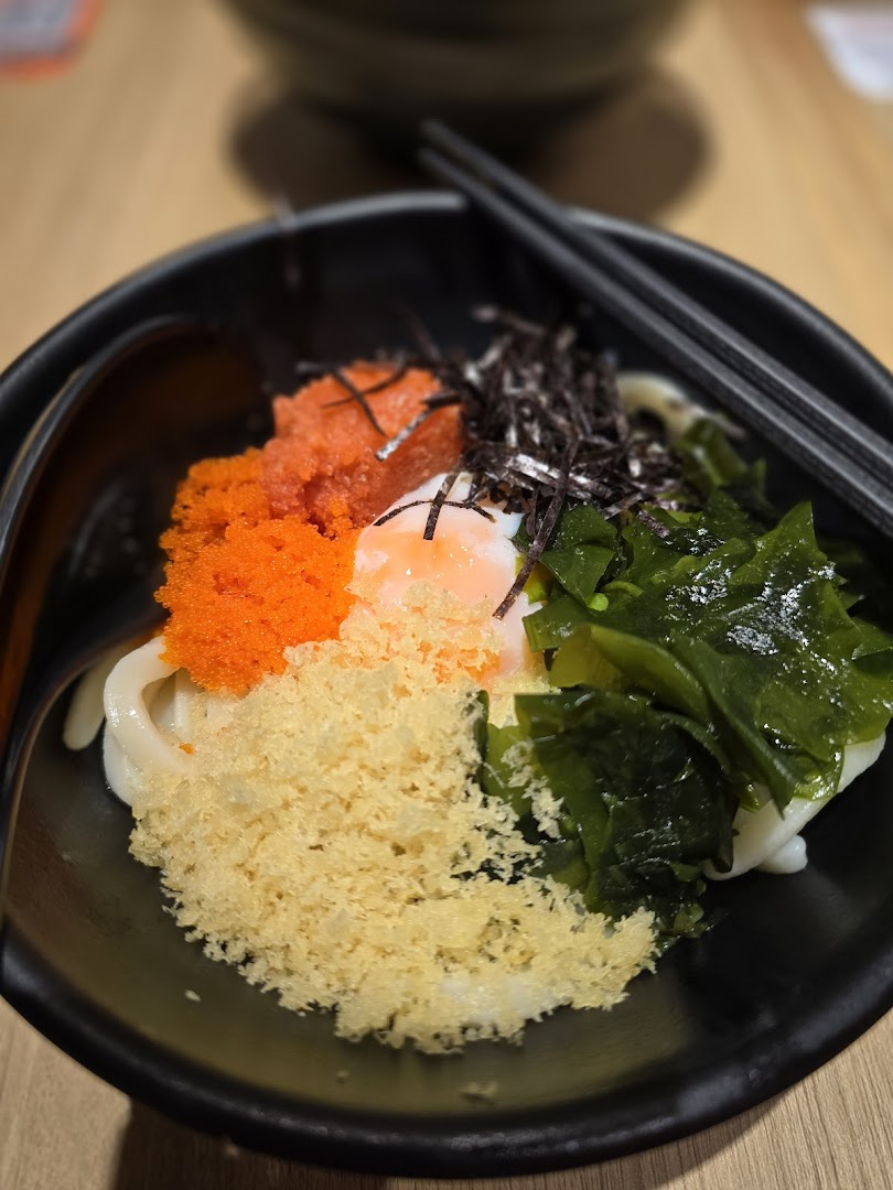 A vibrant bowl of udon noodles topped with tobiko, seaweed, tempura crumbs, and a poached egg.