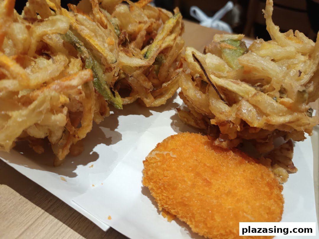 Close-up of crispy Japanese tempura, including kakiage and a breaded item, on a white plate.