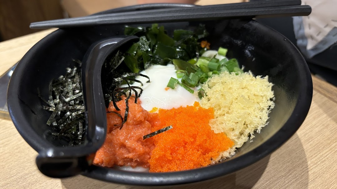 A vibrant bowl of udon with diverse toppings including roe, seaweed, tempura flakes, and a poached egg.