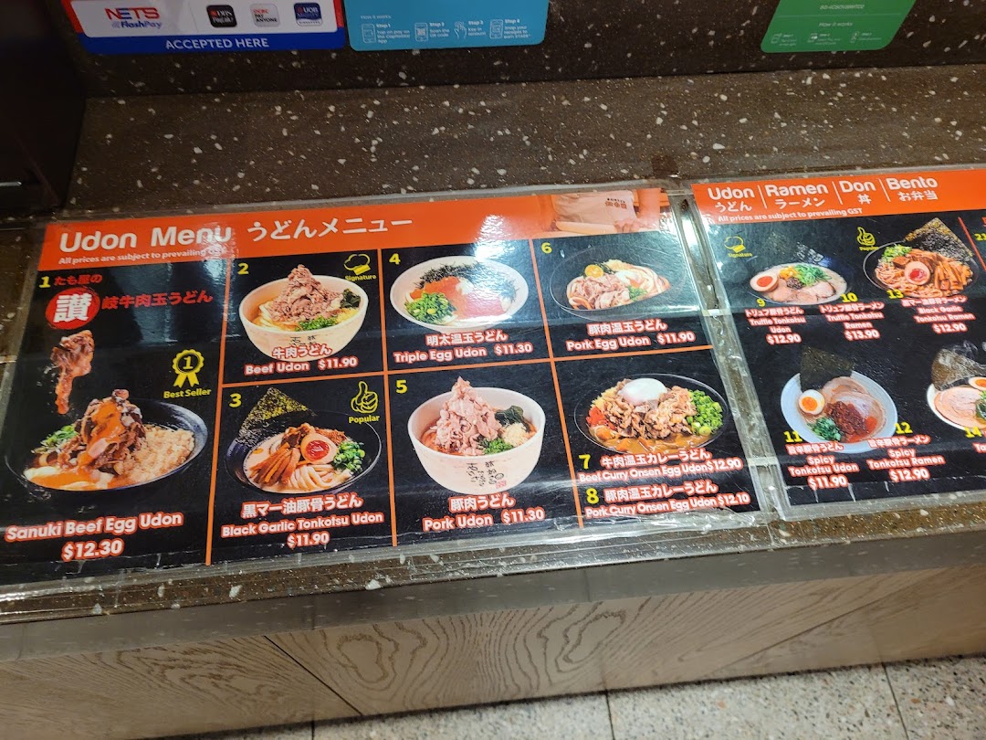 A detailed menu board displaying various udon and ramen dishes with prices and images.