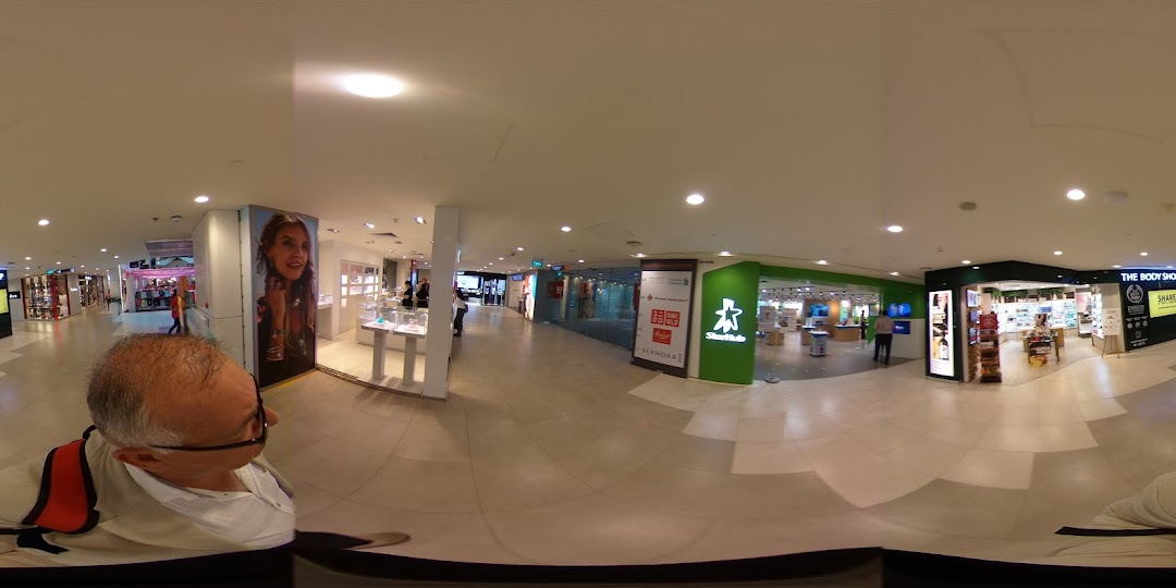 A panoramic view of a brightly lit shopping mall corridor featuring various retail stores, including The Body Shop.