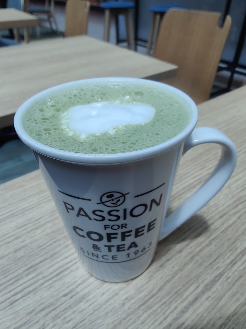 A green tea latte in a branded mug on a wooden table inside the cafe.