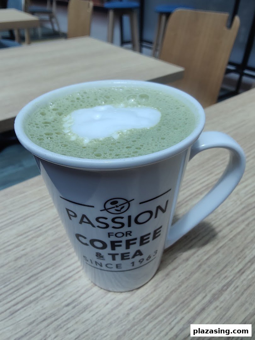 A green tea latte in a branded mug on a wooden table inside the cafe.