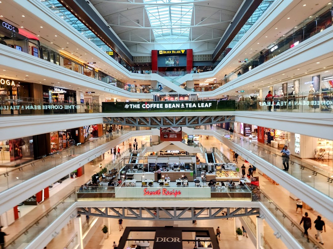 A vibrant multi-level shopping mall interior featuring various retail stores and a prominent 'The Coffee Bean & Tea Leaf' banner.