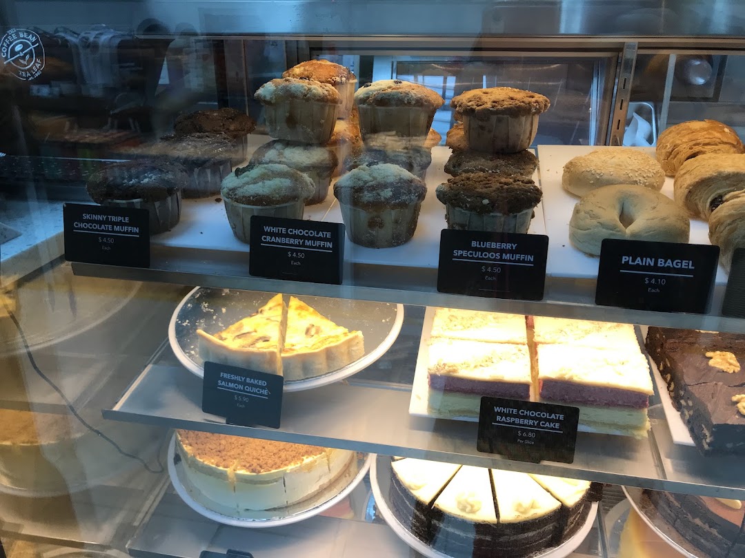 A display case showcasing a variety of freshly baked muffins, bagels, quiche, and cakes.